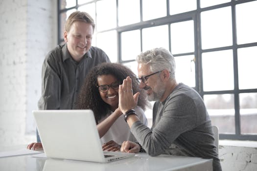 Excited colleagues wearing informal clothes and working on project together while watching video on computer in modern workspace