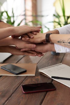 Hands from a diverse team stack on a table symbolizing unity and teamwork in a modern office setting.