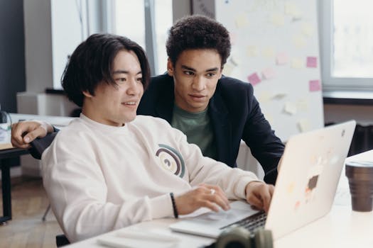 Two diverse young men working together on a laptop in a modern office setting.