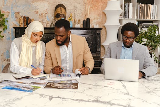 Three colleagues working together on documents and laptop during a meeting.