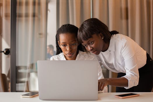 Two African American women working together on a laptop indoors, showcasing teamwork and collaboration.