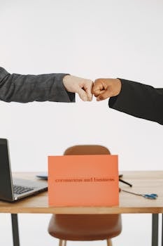 Two businesspeople fist bump over a desk with a sign reading 'coronavirus and business.'