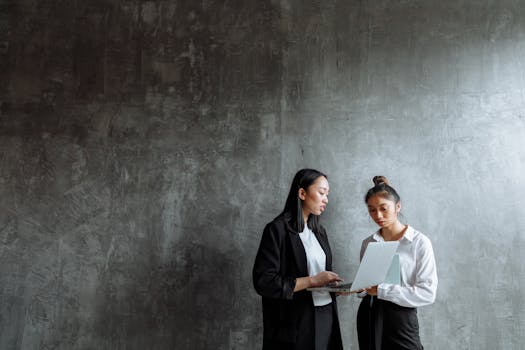 Two professional women collaborating with a laptop in a modern office setting.