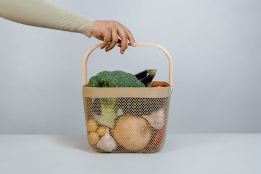 A hand holding a basket filled with fresh vegetables like broccoli and onions.